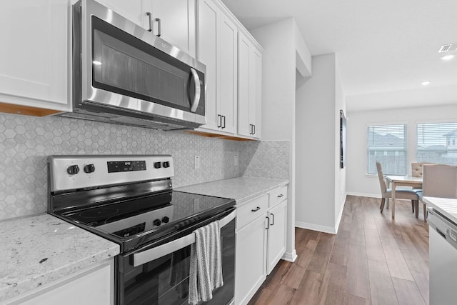 kitchen with white cabinets, wood finished floors, light stone counters, and appliances with stainless steel finishes