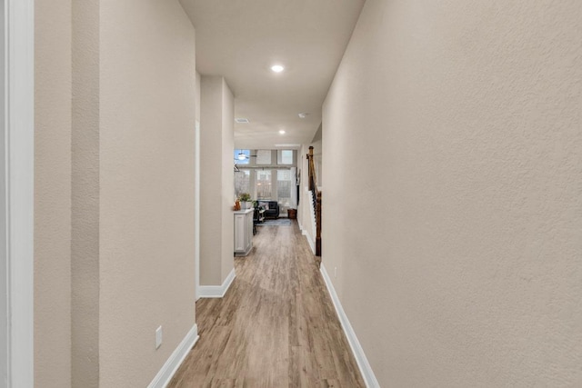 hall featuring light wood-type flooring, baseboards, and recessed lighting
