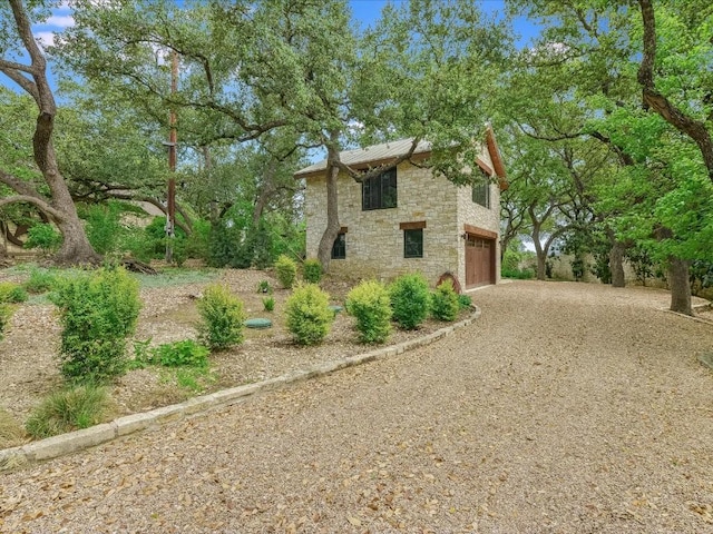 view of side of property featuring driveway, an attached garage, and stone siding