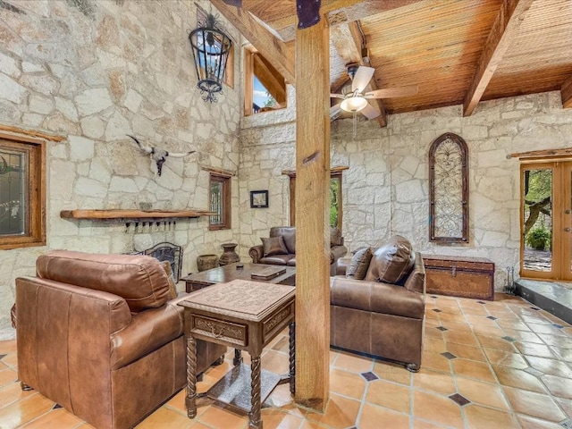 living room with wooden ceiling, tile patterned floors, ceiling fan, a stone fireplace, and beam ceiling