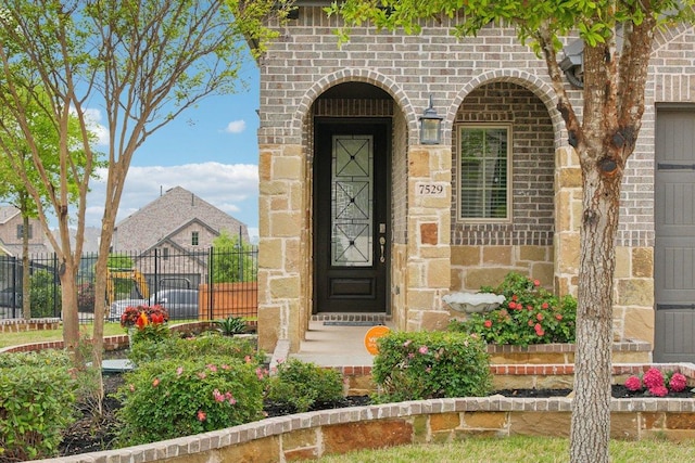 view of exterior entry featuring fence, stone siding, and brick siding