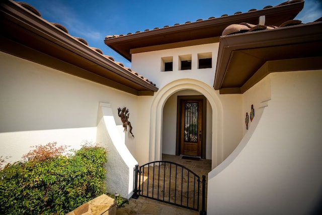 doorway to property featuring stucco siding, a gate, and a tiled roof