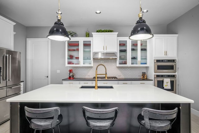 kitchen featuring under cabinet range hood, a center island with sink, backsplash, and appliances with stainless steel finishes