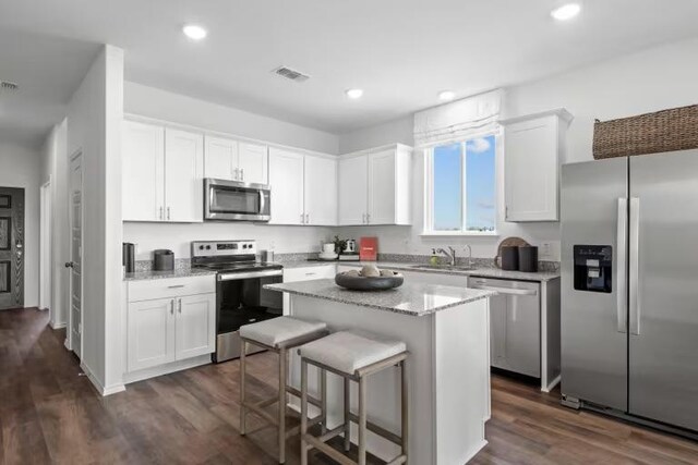 13312 Lapoynor St, Manor, TX 78653 - kitchen with appliances with stainless steel finishes, white cabinets, dark wood finished floors, a kitchen island, and light stone counters