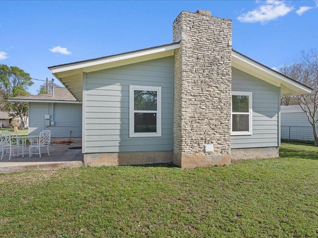 back of house with a lawn, a chimney, and a patio