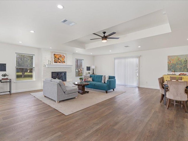 living area with visible vents, wood finished floors, a large fireplace, ceiling fan, and a raised ceiling
