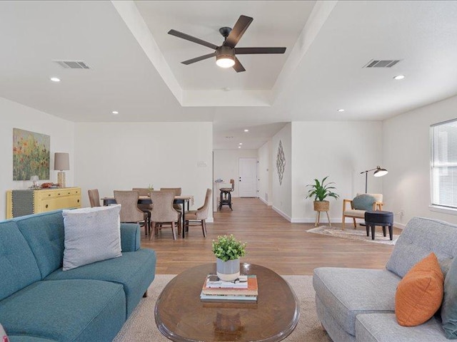 living room featuring light wood-style floors, ceiling fan, a raised ceiling, baseboards, and visible vents