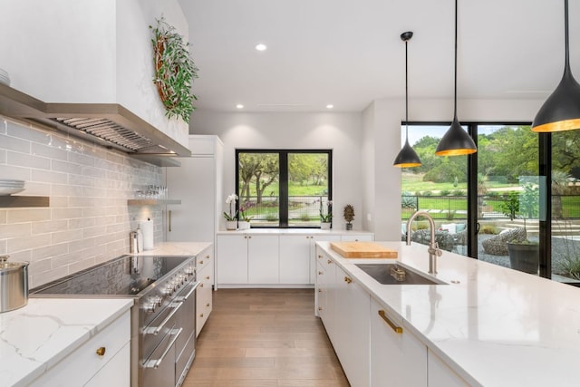 3931 R O Dr, Spicewood, TX 78669 - kitchen featuring a sink, range with two ovens, wall chimney range hood, light wood-style flooring, and plenty of natural light