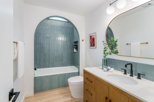 3931 R O Dr, Spicewood, TX 78669 - bathroom featuring vanity, toilet, wood finished floors, tiled shower / bath combo, and tasteful backsplash