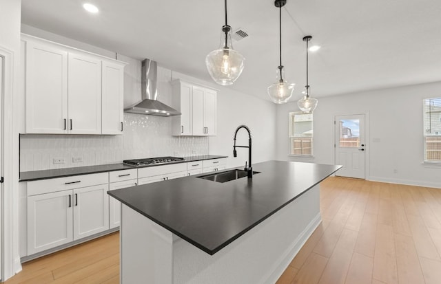 16824 Santiaguillo Trce, Manor, TX 78653 - kitchen with wall chimney range hood, stainless steel gas cooktop, tasteful backsplash, dark countertops, and a kitchen island with sink