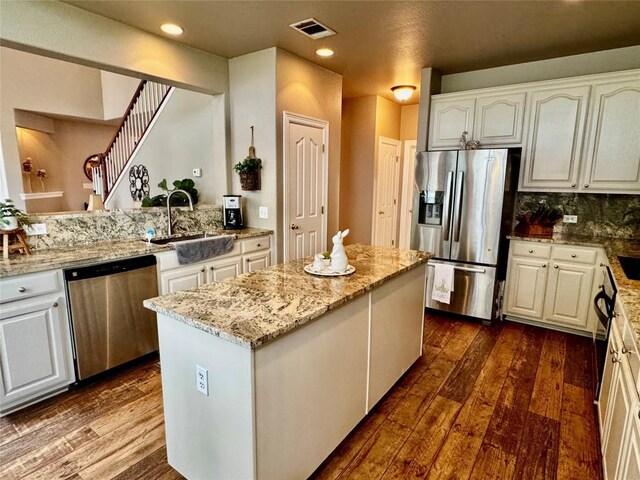 30105 Meadow Greens Dr, Georgetown, TX 78628 - kitchen featuring appliances with stainless steel finishes, dark wood-type flooring, white cabinetry, a kitchen island, and light stone countertops