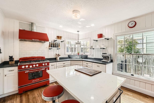 811 E 45th St, Austin, TX 78751 - kitchen featuring stainless steel range, wall chimney range hood, a textured ceiling, light wood-style flooring, and open shelves