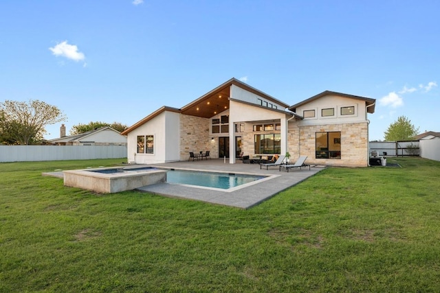 rear view of house with stone siding, a fenced backyard, an in ground hot tub, and a lawn