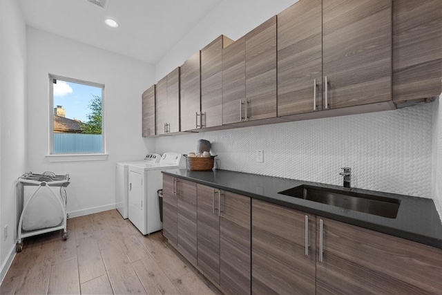 laundry room featuring baseboards, a sink, light wood-style floors, washer and dryer, and cabinet space