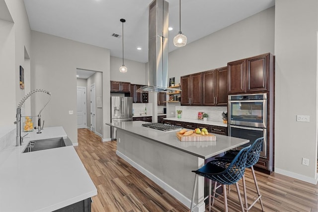 kitchen featuring island range hood, stainless steel appliances, decorative backsplash, a sink, and dark brown cabinetry