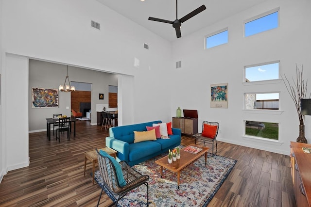 living room featuring ceiling fan with notable chandelier, visible vents, baseboards, and dark wood-style flooring