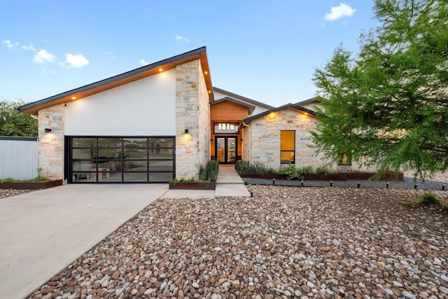 modern home with stone siding, driveway, french doors, and an attached garage