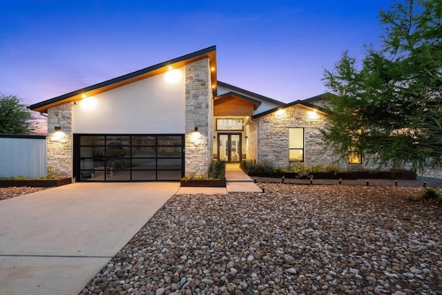 modern home featuring stone siding, driveway, french doors, and an attached garage