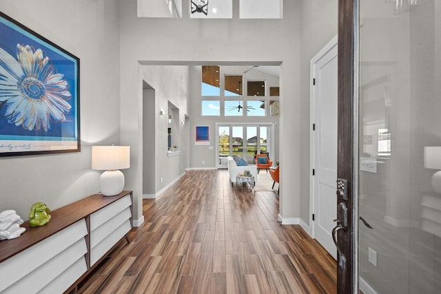 foyer featuring a high ceiling, baseboards, ceiling fan, and wood finished floors