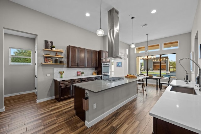 kitchen featuring island range hood, dark wood finished floors, backsplash, a sink, and dark brown cabinetry