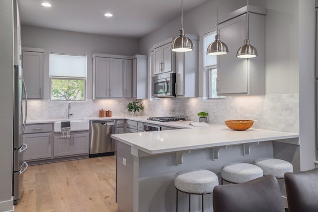 2513 Moreno St, Austin, TX 78723 - kitchen with stainless steel appliances, a peninsula, gray cabinetry, a sink, and light wood-style floors