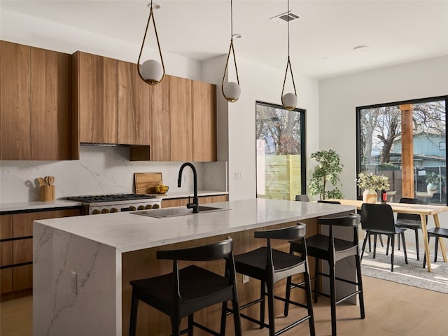 3210 Thompson, Austin, TX 78702 - kitchen featuring modern cabinets, a sink, backsplash, brown cabinetry, and a center island with sink