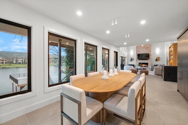 dining area featuring recessed lighting, light tile patterned flooring, a water view, and a fireplace