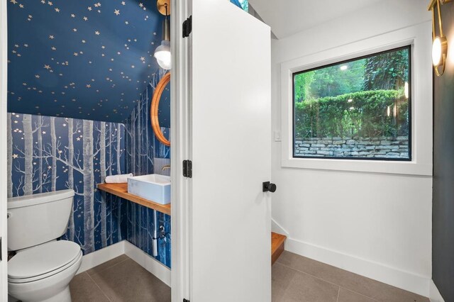 half bathroom featuring toilet, tile patterned floors, wallpapered walls, a sink, and baseboards