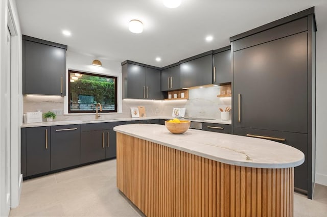 kitchen with decorative backsplash, light stone countertops, a sink, and a kitchen island