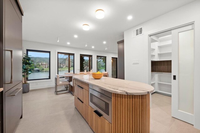 kitchen with modern cabinets, stainless steel appliances, light stone countertops, visible vents, and a kitchen island