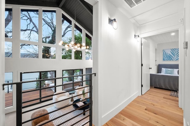 hall with visible vents, baseboards, an inviting chandelier, a towering ceiling, and wood finished floors