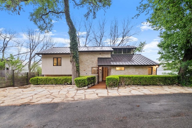 view of front of house featuring a standing seam roof, fence, stone siding, and metal roof