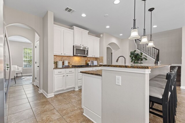 3312 Cortes Pl, Round Rock, TX 78665 - kitchen with stainless steel appliances, arched walkways, a kitchen bar, decorative backsplash, and white cabinetry