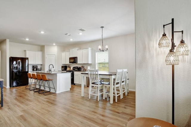 118 Esparza Dr, Bastrop, TX 78602 - kitchen with black appliances, a chandelier, light wood-style flooring, white cabinetry, and recessed lighting