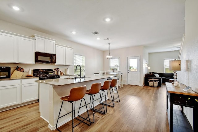 118 Esparza Dr, Bastrop, TX 78602 - kitchen with black microwave, gas range, a breakfast bar area, an island with sink, and white cabinetry