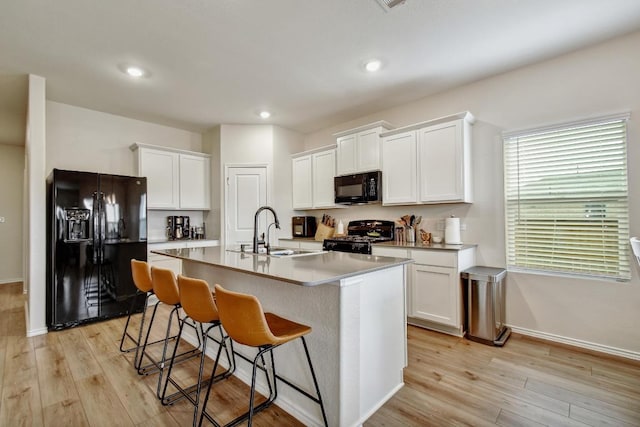 118 Esparza Dr, Bastrop, TX 78602 - kitchen featuring black appliances, a breakfast bar area, light wood-style flooring, an island with sink, and recessed lighting