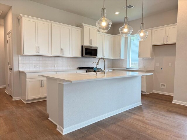 8516 Dongan Dr, Austin, TX 78744 - kitchen with stainless steel microwave, dark wood finished floors, white cabinets, a kitchen island with sink, and recessed lighting