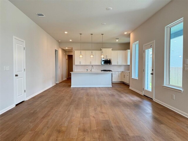 8516 Dongan Dr, Austin, TX 78744 - kitchen featuring stainless steel microwave, decorative backsplash, plenty of natural light, wood finished floors, and recessed lighting