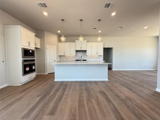 8600 Dongan Dr, Austin, TX 78744 - kitchen with stainless steel appliances, decorative backsplash, white cabinets, light countertops, and an island with sink