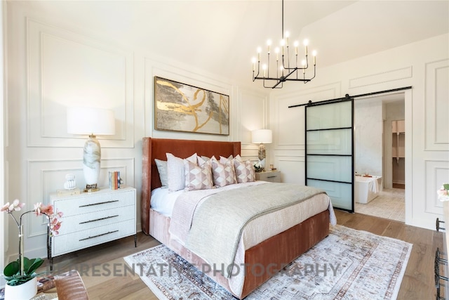 bedroom with a decorative wall, a barn door, a notable chandelier, and dark wood-style flooring