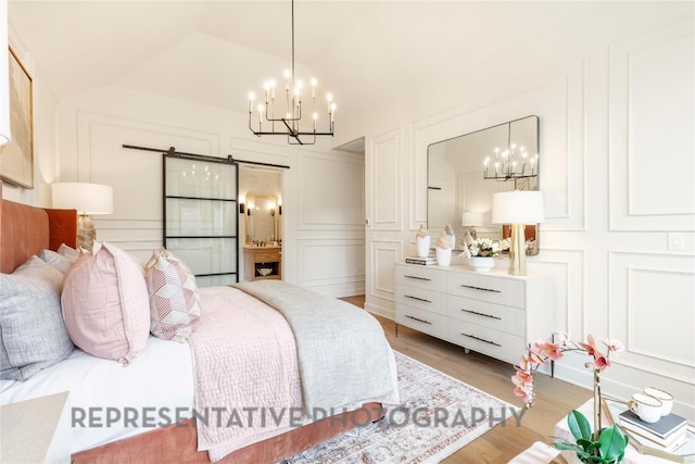 bedroom with a notable chandelier, vaulted ceiling, light wood-style flooring, a barn door, and a decorative wall