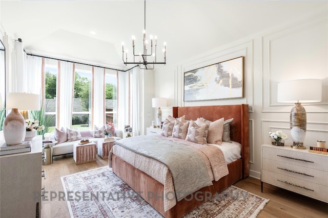 bedroom featuring light wood finished floors, an inviting chandelier, and vaulted ceiling