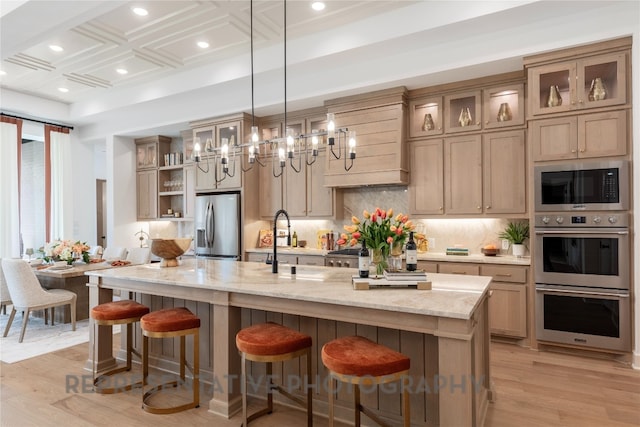kitchen with appliances with stainless steel finishes, a large island, light wood-style floors, decorative backsplash, and a sink