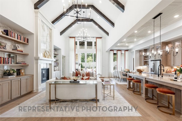 living area featuring beam ceiling, high vaulted ceiling, an inviting chandelier, and light wood finished floors