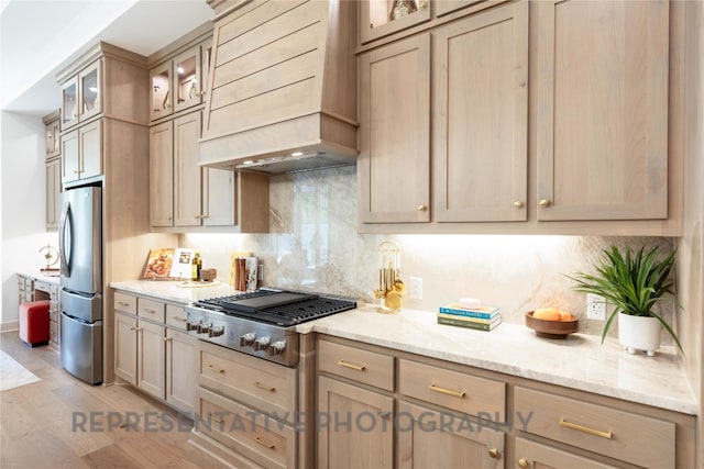 kitchen featuring custom exhaust hood, light stone countertops, light wood-style floors, decorative backsplash, and stainless steel appliances