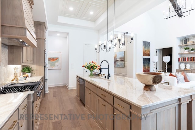 kitchen featuring stainless steel appliances, a sink, premium range hood, and an inviting chandelier