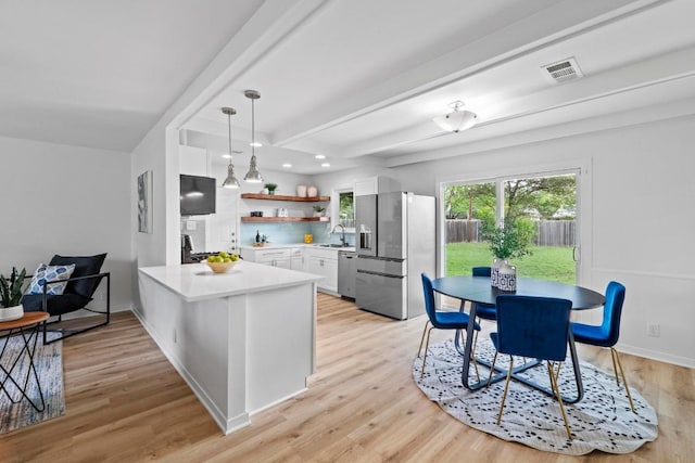 7003 Priscilla Dr, Austin, TX 78752 - kitchen featuring appliances with stainless steel finishes, a peninsula, white cabinetry, light wood-style flooring, and light countertops