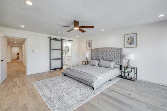 313 Lucy Ln, Horseshoe Bay, TX 78657 - bedroom with a barn door, light wood-type flooring, a textured ceiling, recessed lighting, and baseboards