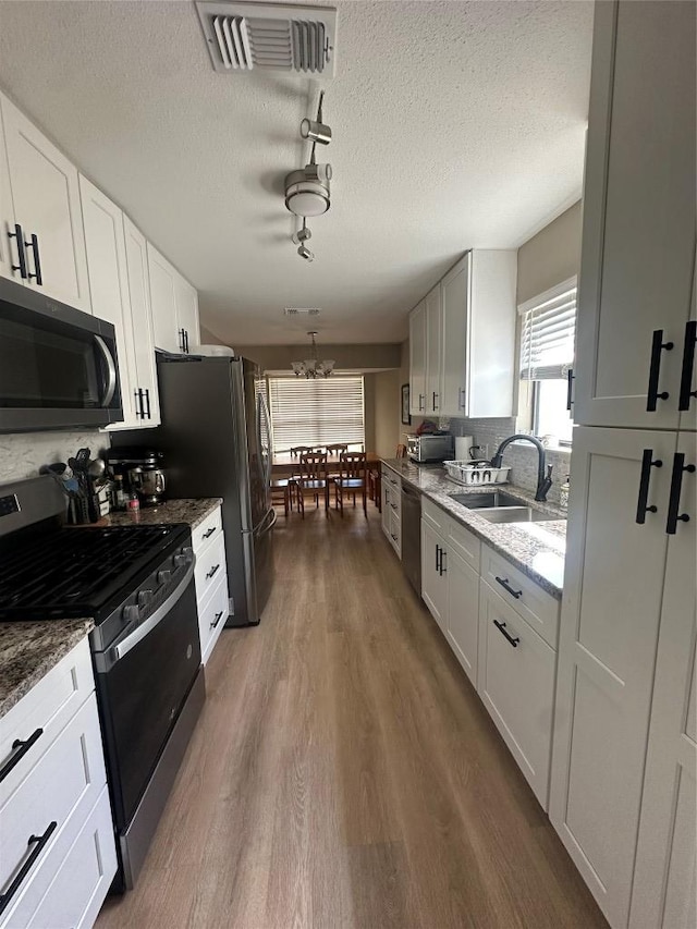 513 Purple Sage Dr, Round Rock, TX 78681 - kitchen with appliances with stainless steel finishes, wood finished floors, a textured ceiling, white cabinets, and light stone countertops