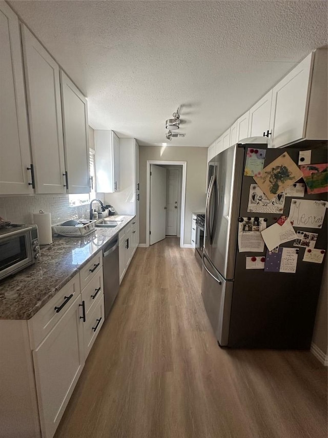 513 Purple Sage Dr, Round Rock, TX 78681 - kitchen with appliances with stainless steel finishes, light wood-type flooring, white cabinets, a textured ceiling, and tasteful backsplash